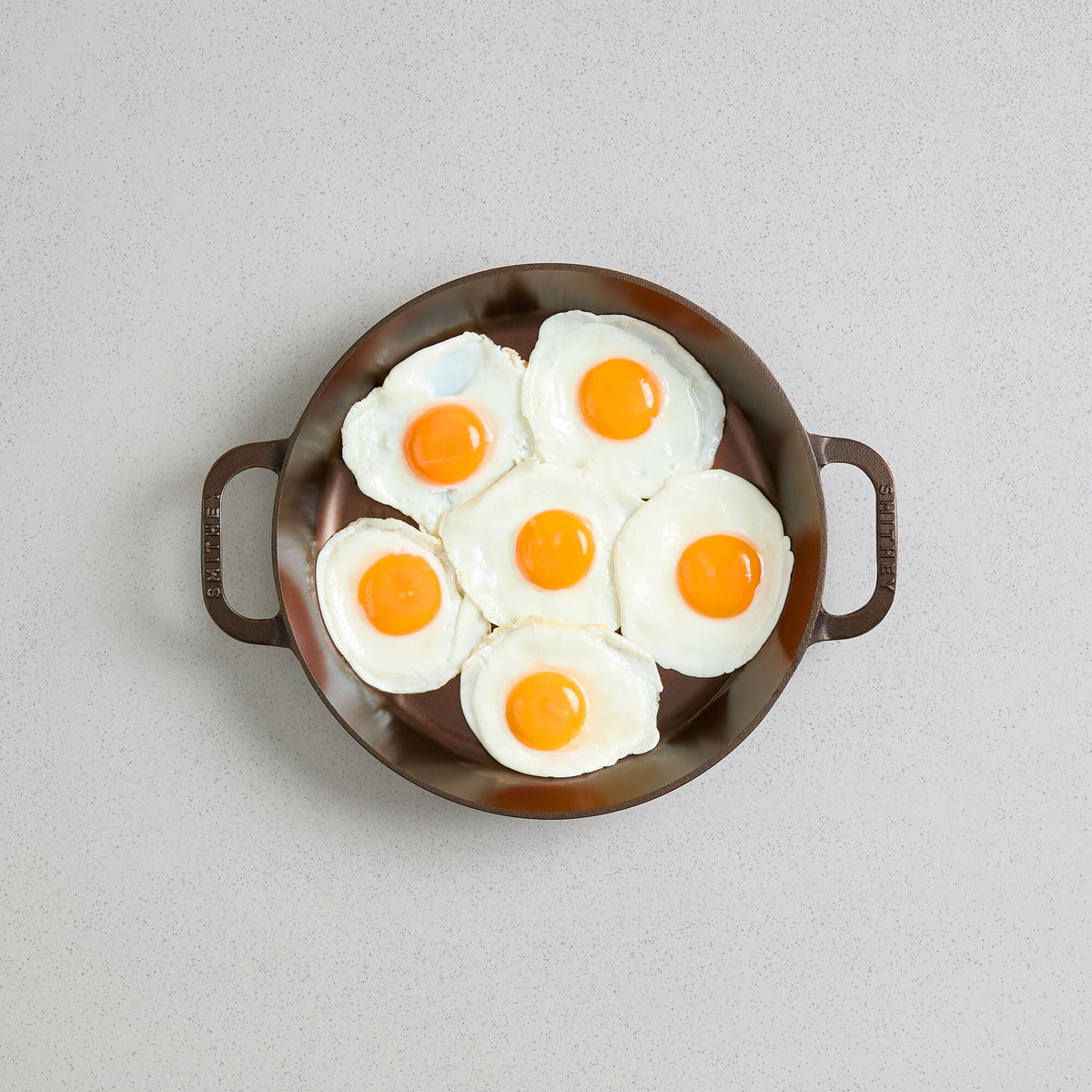 Seven fried eggs in a No. 12 Dual Handle Skillet, viewed from above