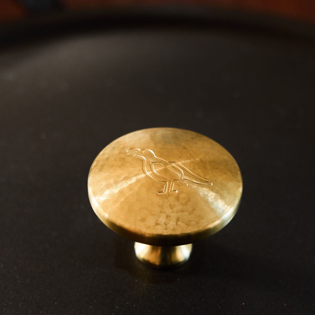 Close-up of the hand-hammered brass knob on The Carbon Steel Lid, stamped with the Smithey bird