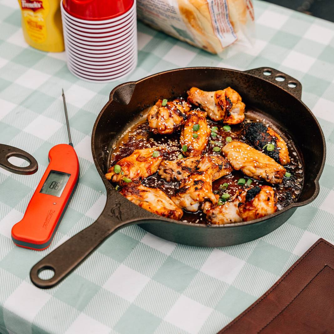 Chicken thighs in a No. 10 Skillet next to a meat thermometer on a picnic table