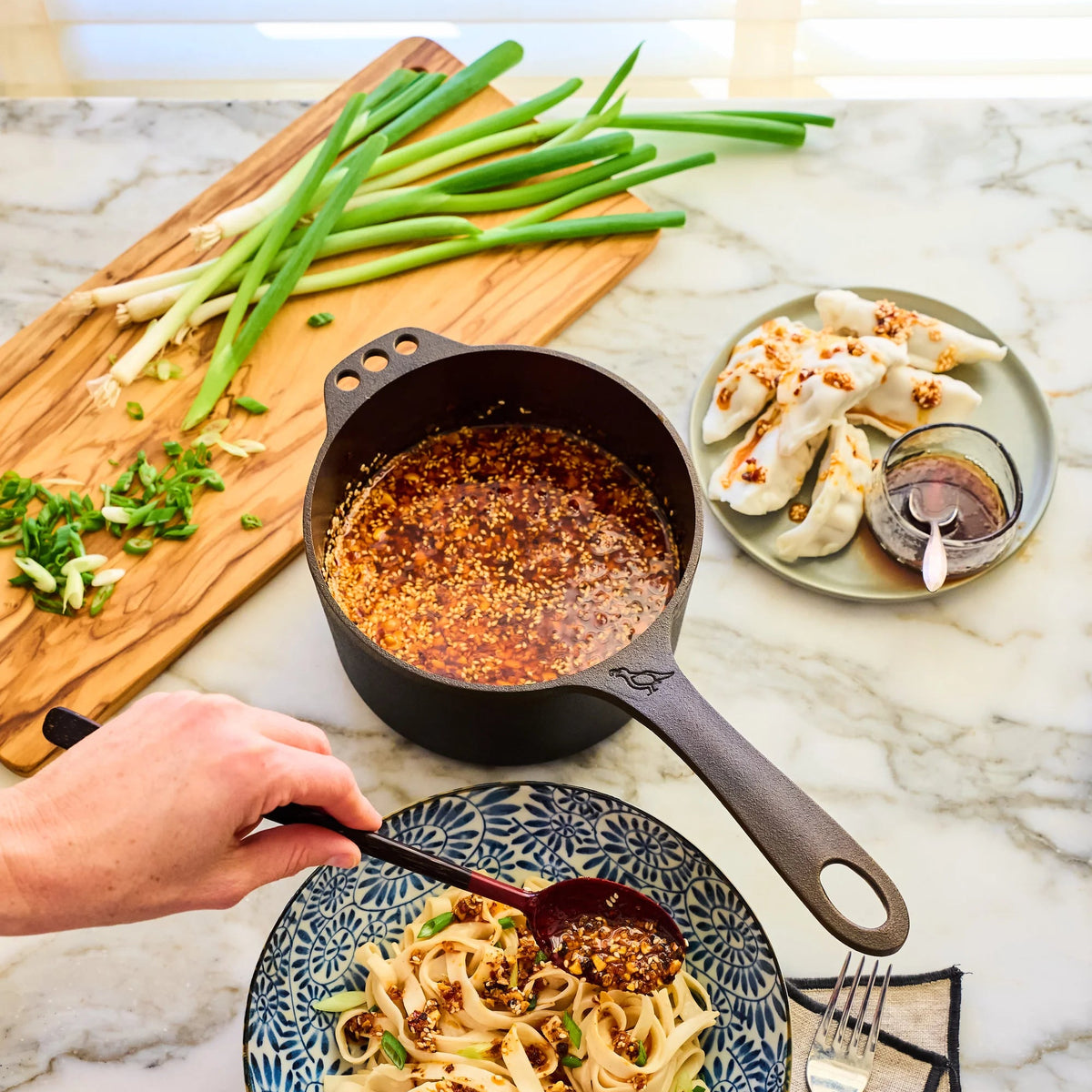 Meat sauce in a 1 Qt Saucepan being ladled over noodles on a marble counter