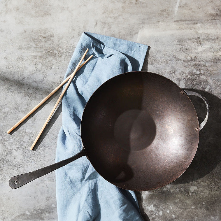 A seasoned Wok with wooden chopsticks on a blue linen napkin