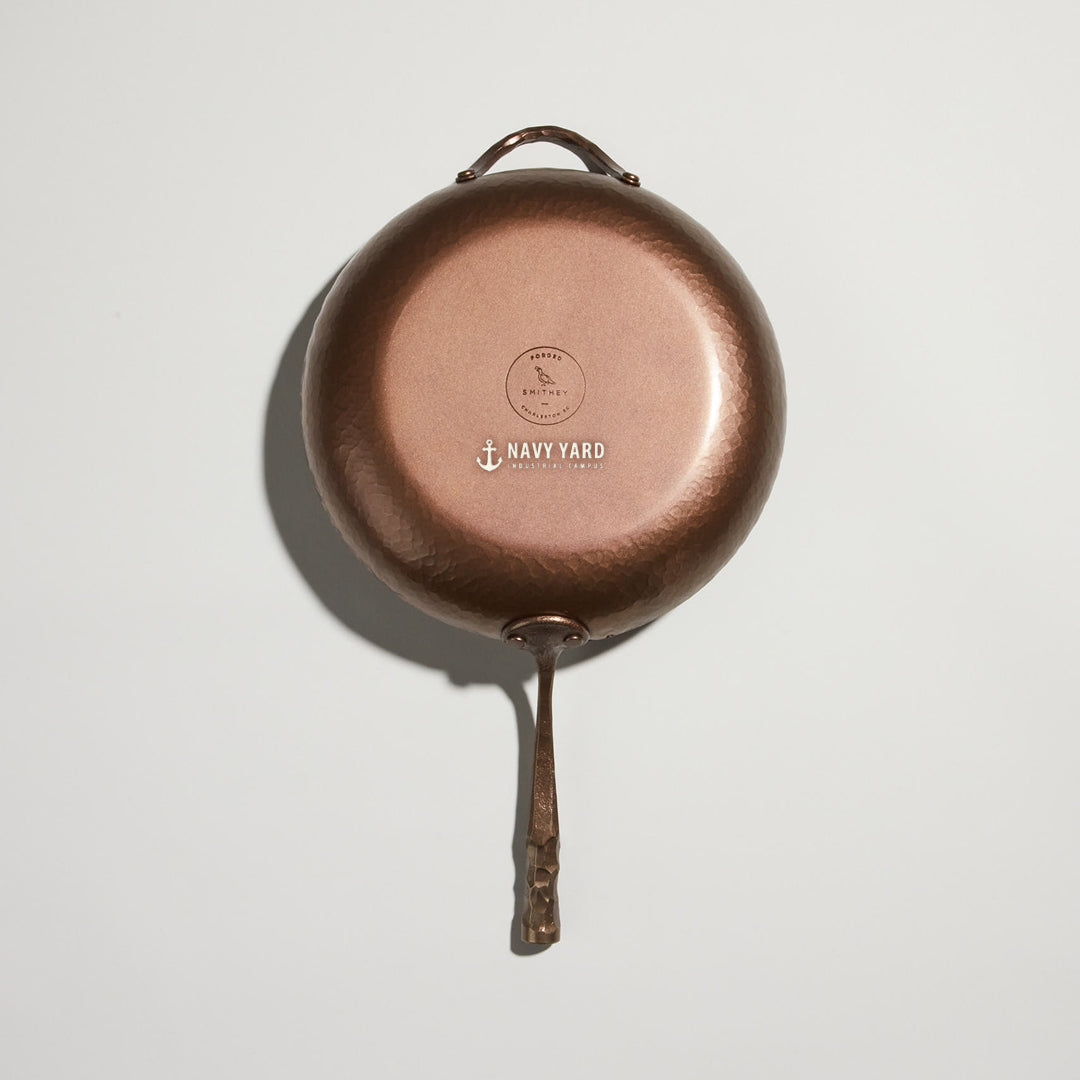 Close crop of a carbon steel skillet base with a client logo engraved beside the Smithey mark