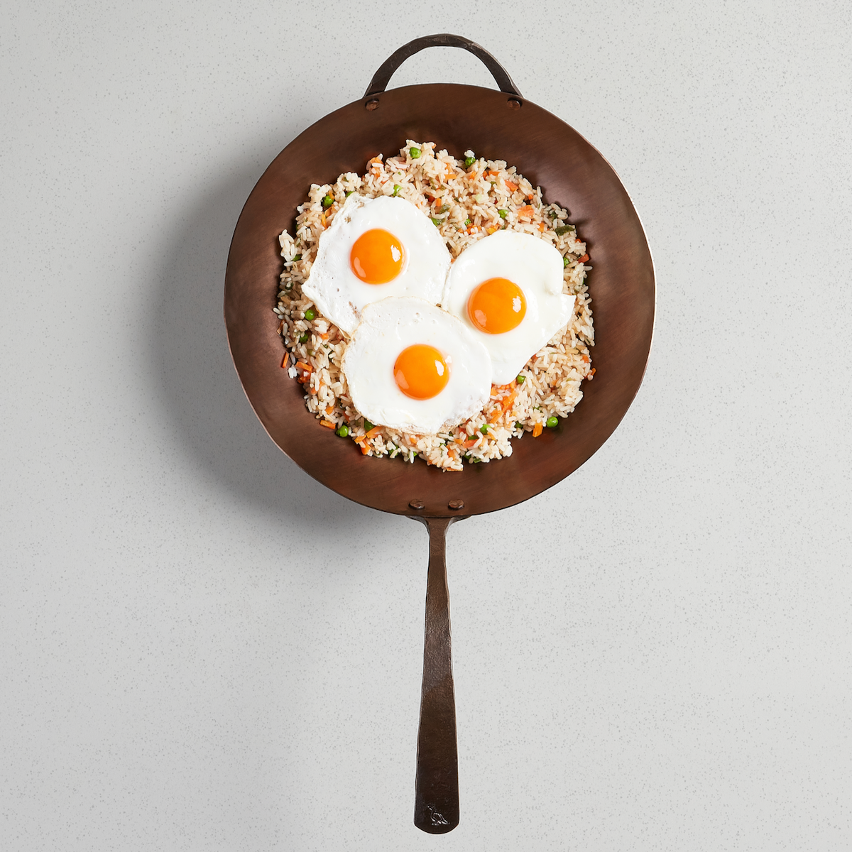 Fried eggs over fried rice in a Wok, viewed from above